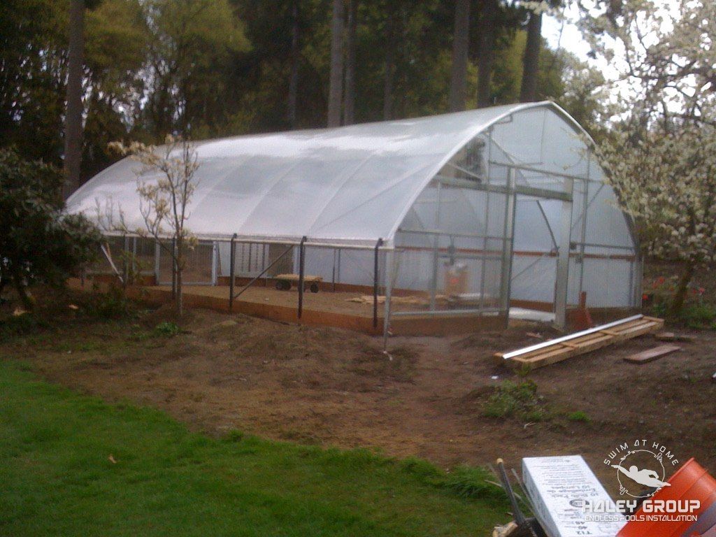 Residential hoop-style greenhouse on a timber base in a wooded yard