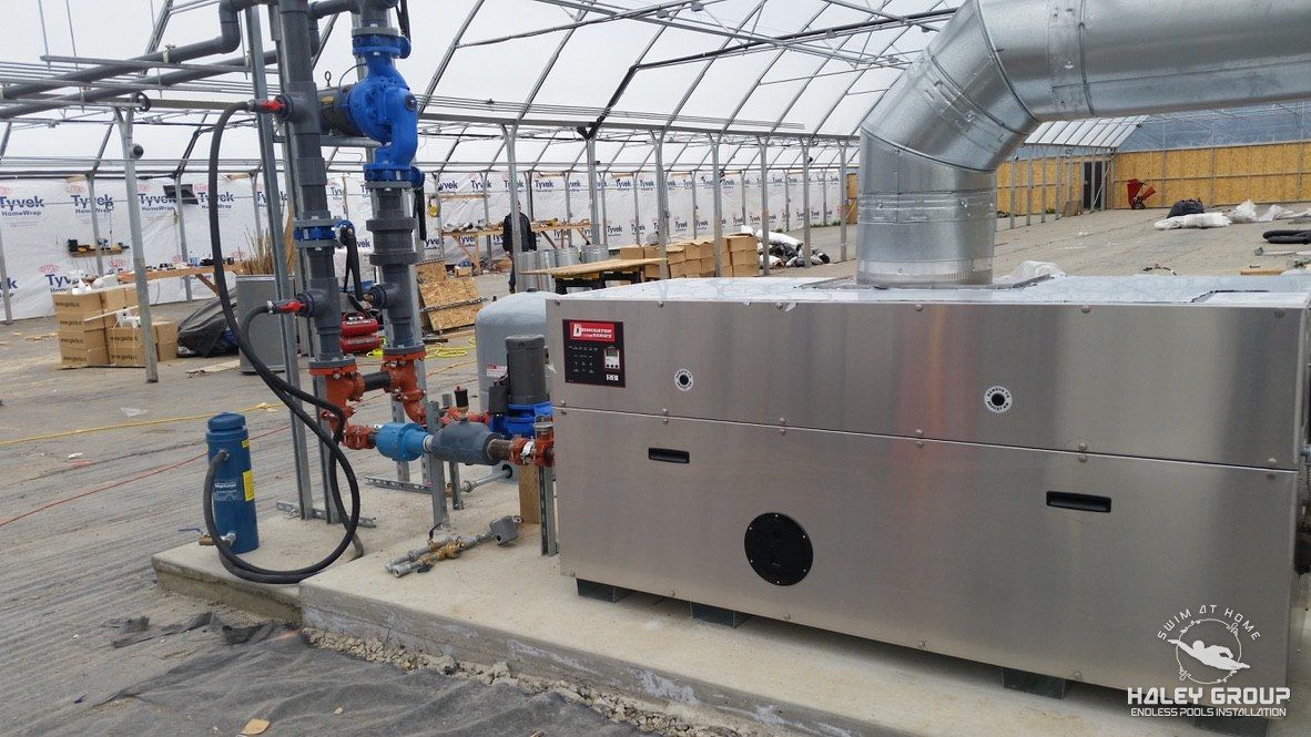 Stainless heating boiler with piping and flue installed on a concrete pad inside a greenhouse