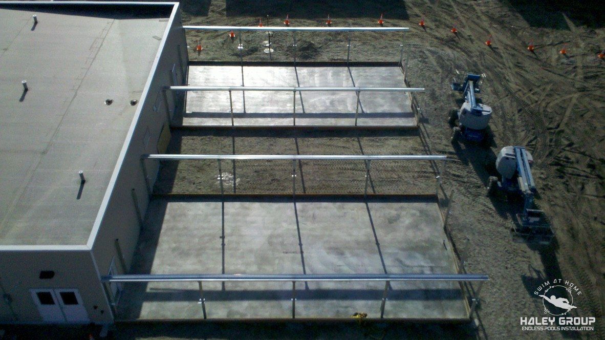 Aerial view of greenhouse framing going up on new slabs beside a building