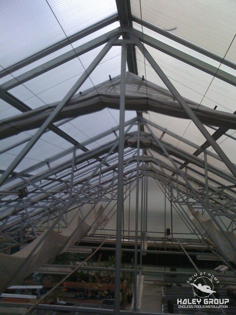 Looking up into the steel truss framing of a glazed gable greenhouse